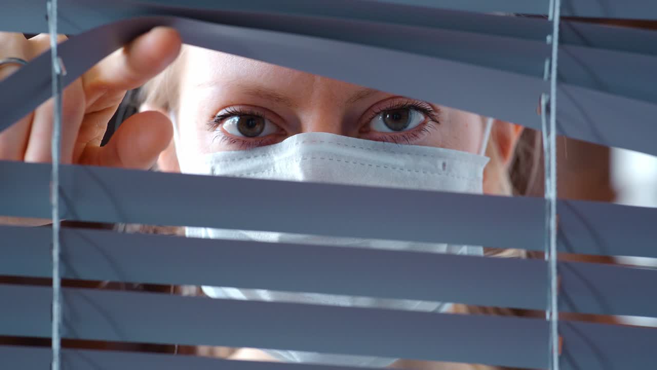 Woman Looking Through Blinds Wearing a Face Mask