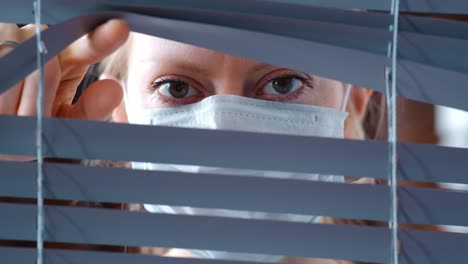 woman looking through blinds wearing a face mask
