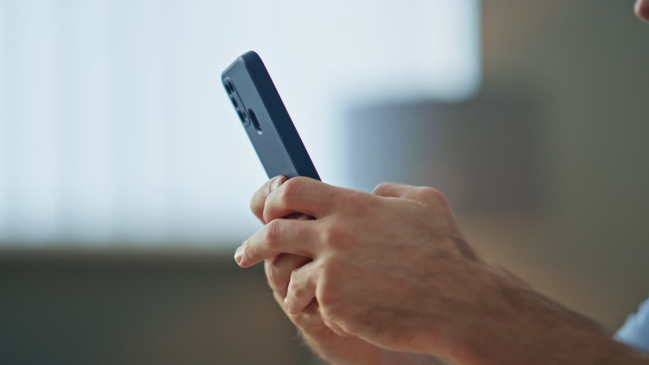 Closeup man hands texting cellphone in apartment. Businessman looking smartphone