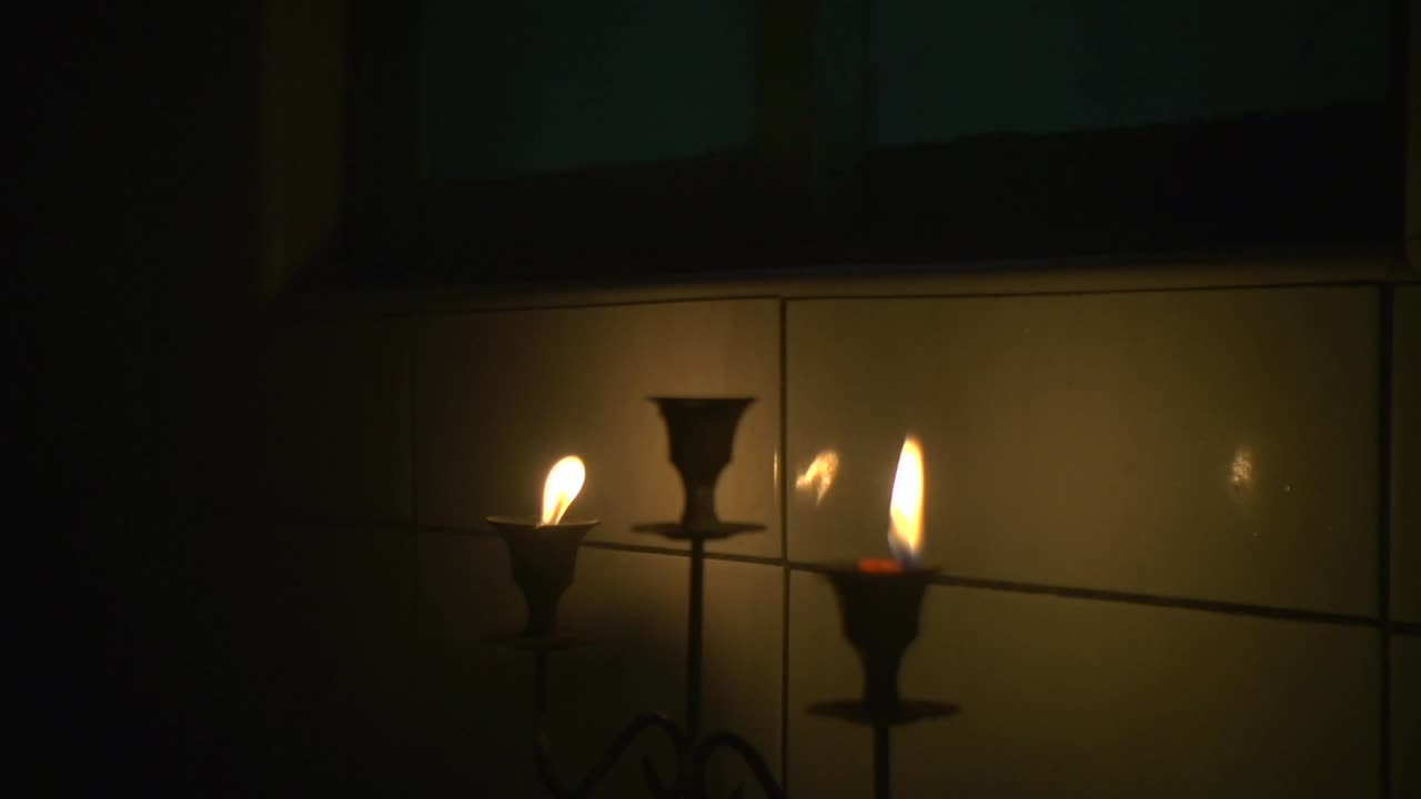 Two candles on candle holder lit and placed near tiled wall for warm and cozy ethereal feeling, filmed as close up
