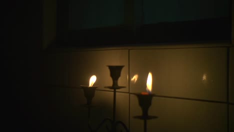 two candles on candle holder lit and placed near tiled wall for warm and cozy ethereal feeling, filmed as close up