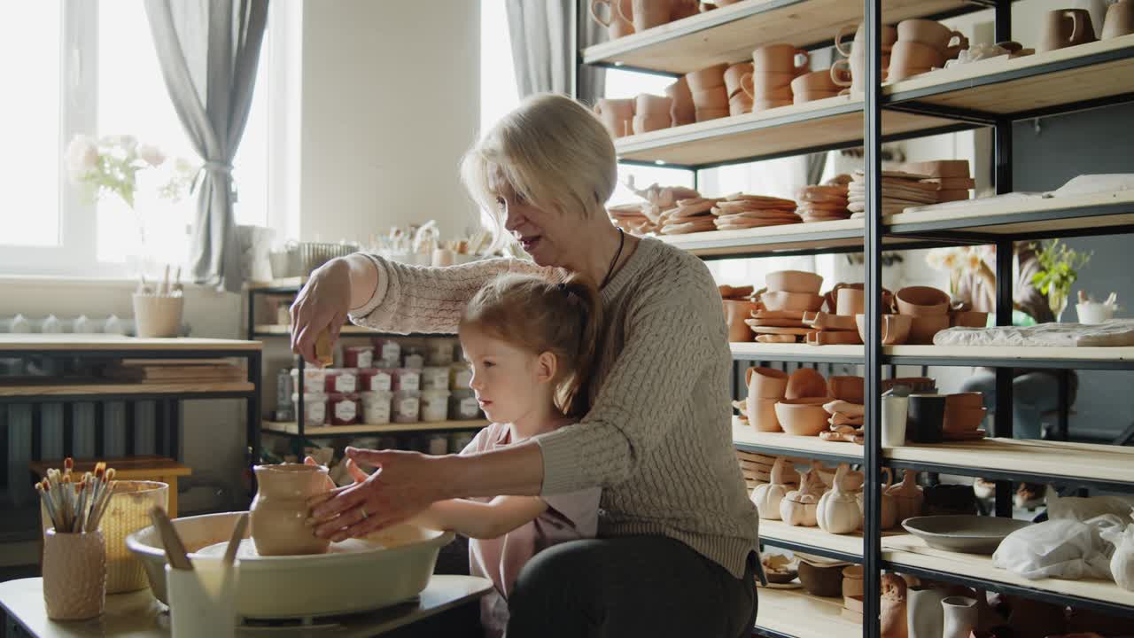 la abuela enseña a su nieta a trabajar en una rueda giratoria de cerámica