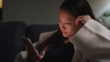 close up of woman spending evening at home sitting on sofa with mobile phone scrolling through internet or social media 7