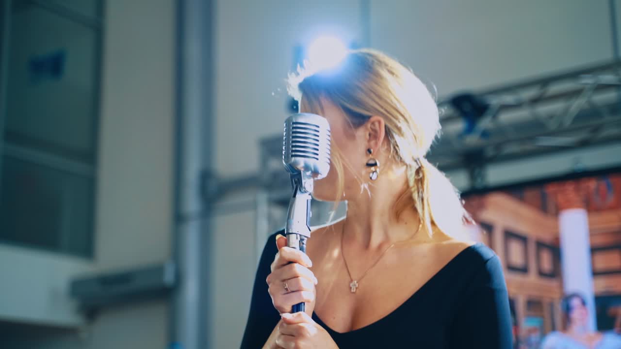 Attractive woman singing into a mic. Professional singer standing at the microphone and performing a live music. Slow motion.
