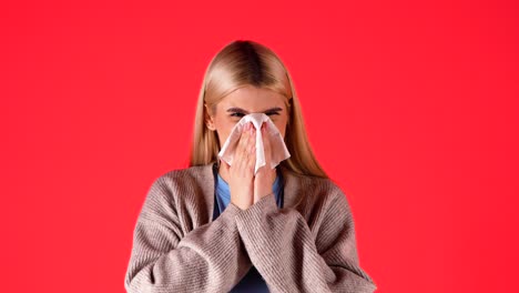 sick blonde woman sneezes in handkerchief, concept allergic to hay, red background