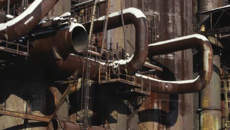 Part-of-an-industrial-plant-with-large-rusted-old-pipes-connected-to-rusted-tanks-partially-covered-with-snow