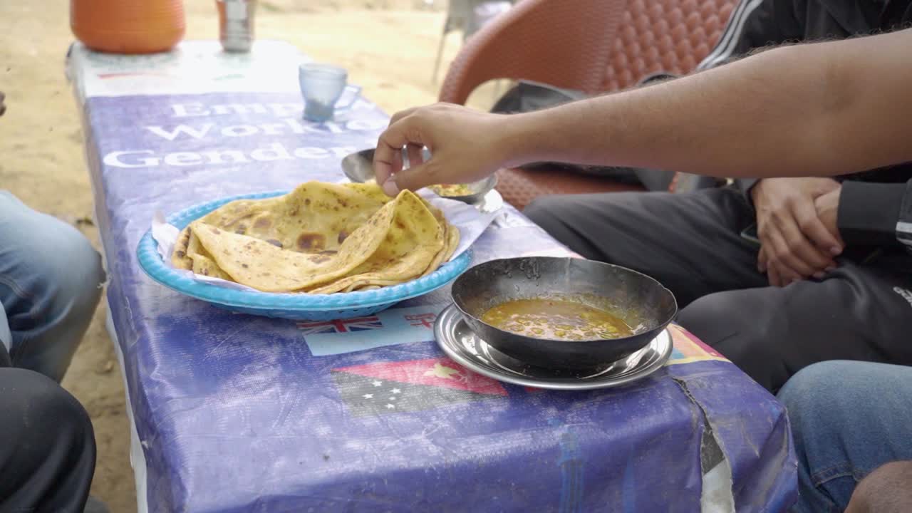 People relish a delightful breakfast at a charming local dhaba, which features warm, crispy parathas, flavorful omelets, tea, and refreshing raita.