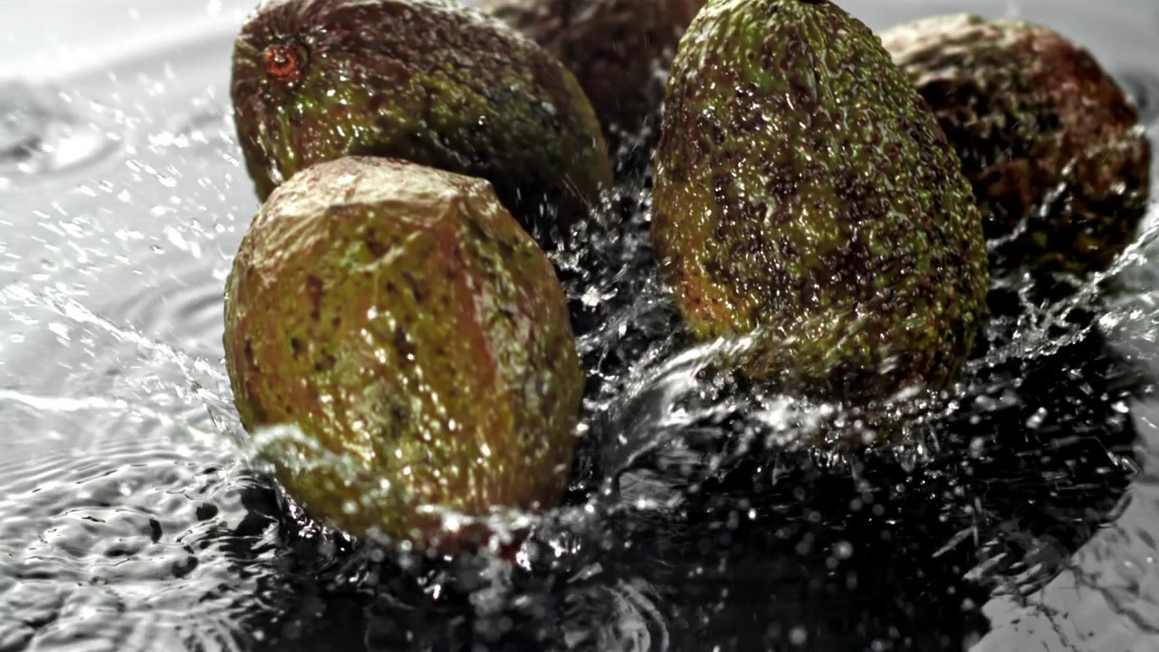Friske avocadoer falder ned i vand med plask i slowmotion