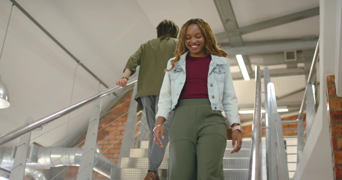 Afroamerikanske kolleger passerer hinanden på metaltrapper, kvinde går ned efter at have passeret manden på vej til arbejde.