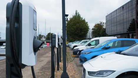 Two-electric-cars-charging-on-a-city-street,-a-cable-connected-to-a-car,-future-of-the-automobile,-clean-sustainable-energy,-overcast-day,-medium-shot