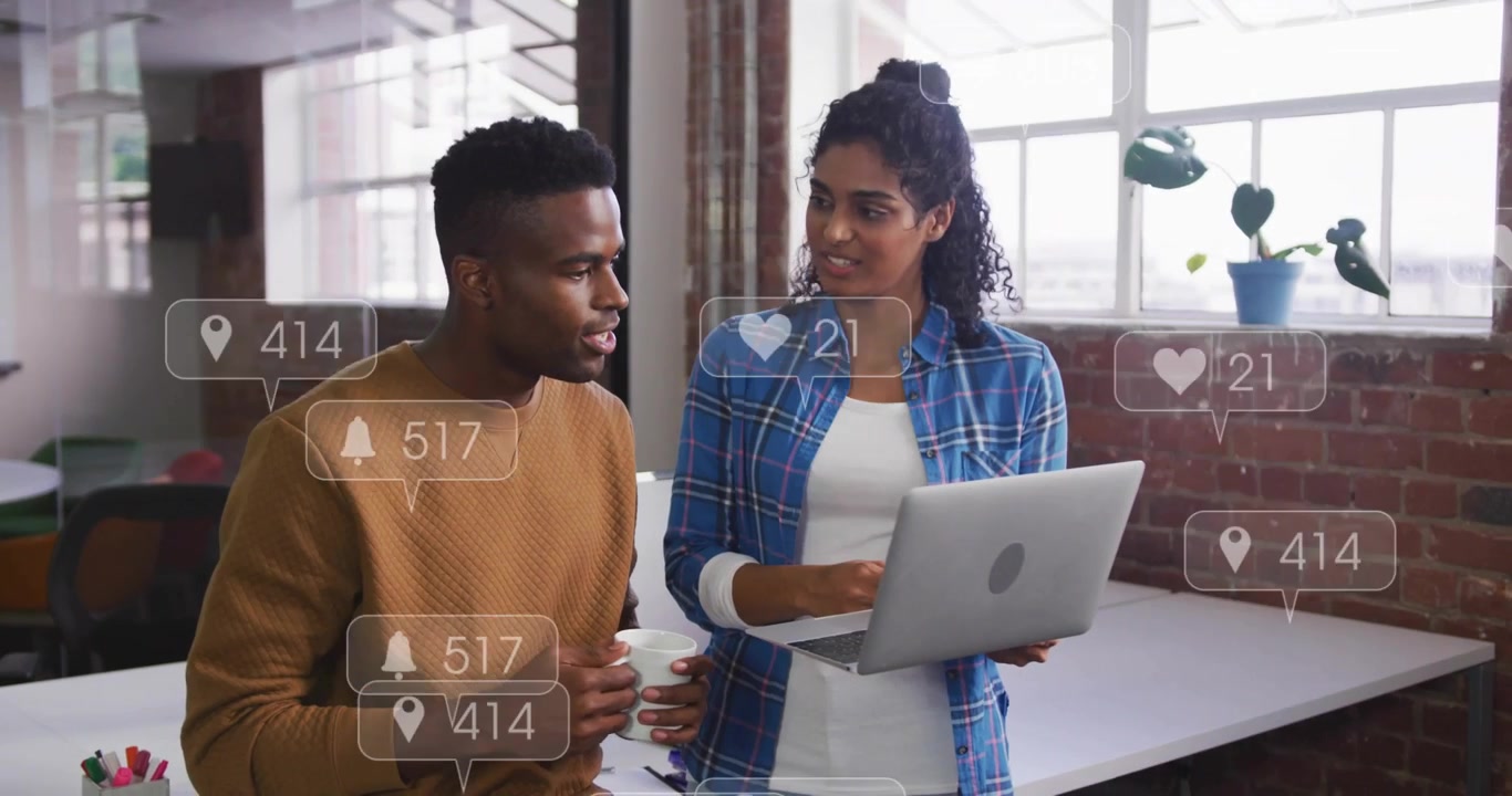 Notifications appearing, pair reviewing silver laptop in open office with white mug, in plaid shirt