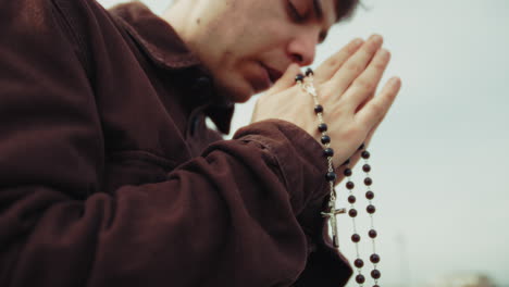 hands of a religious man praying with a rosary and crucifix