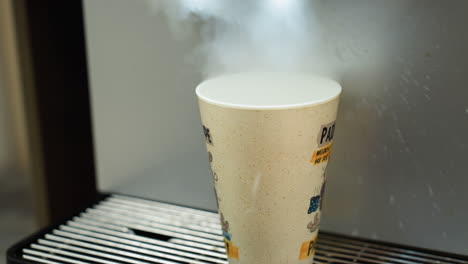 view of hot water being poured into a coffee cup from a machine. the video is shot with a handheld camera, capturing the detailed process of filling the cup with steaming water