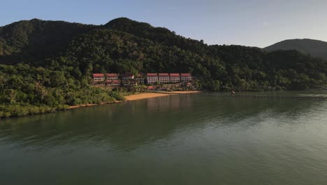 slow aerial shot above the pacific ocean with a pier and resort in the distance on the rainforest island of koh chang, thailand