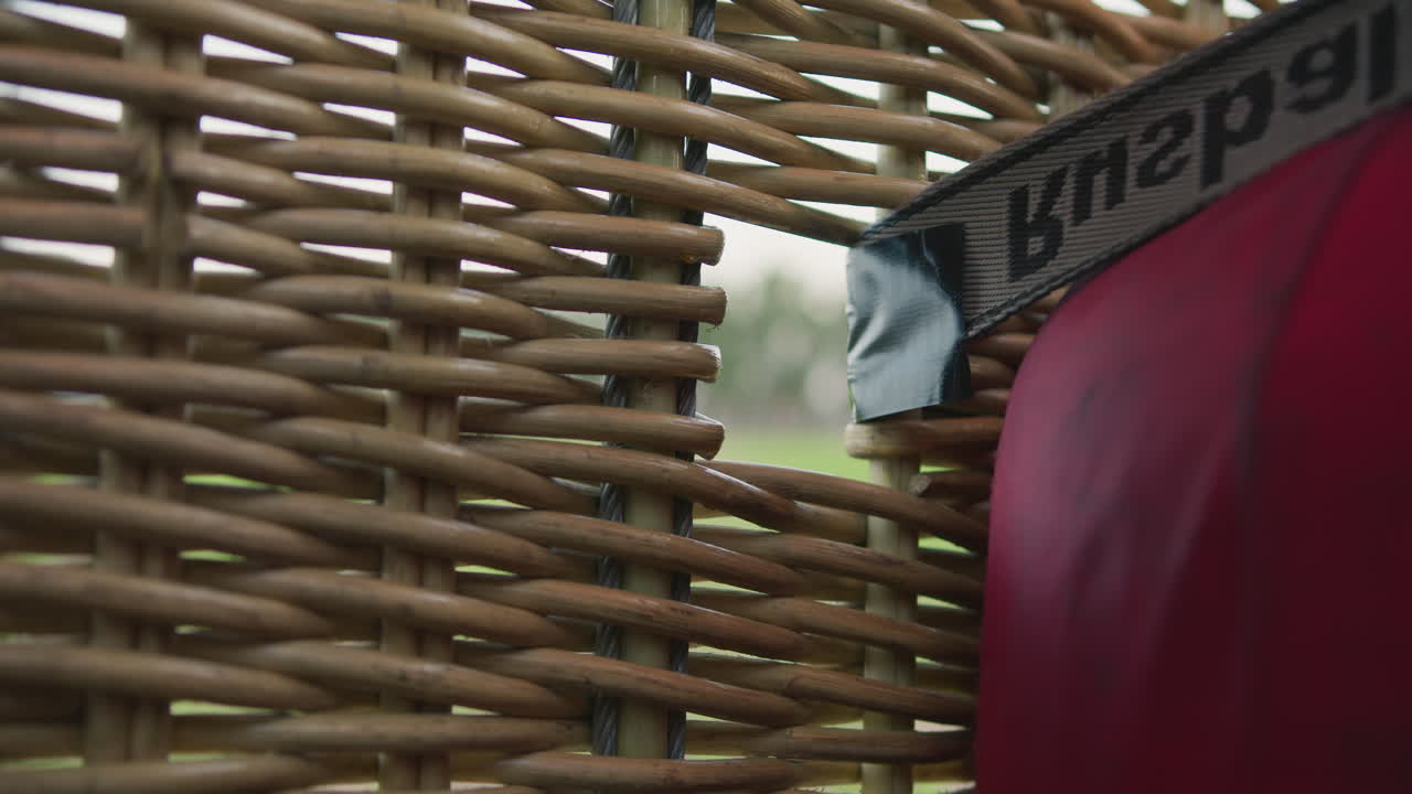 close up detail of woven wicker structure on hot air balloon basket with blurred green landscape in background and black strap partially taped to edge adding rustic