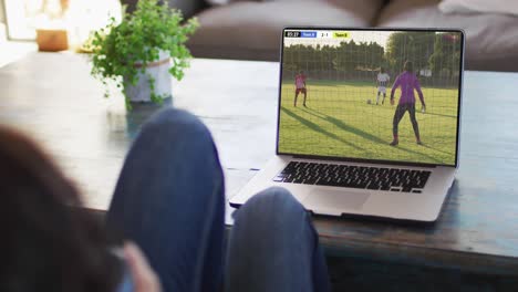 man using laptop with diverse male soccer players playing match on screen