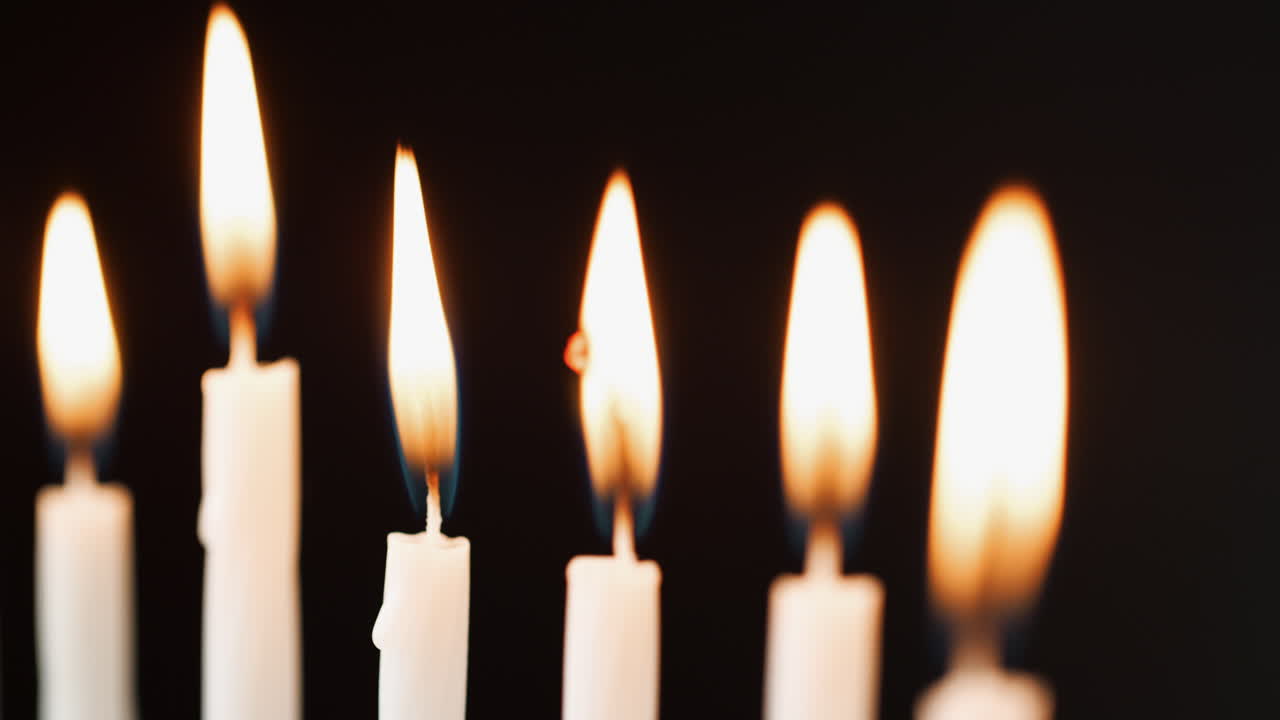 Primo piano di sei candele bianche accese che bruciano in fila, con messa a fuoco selettiva.