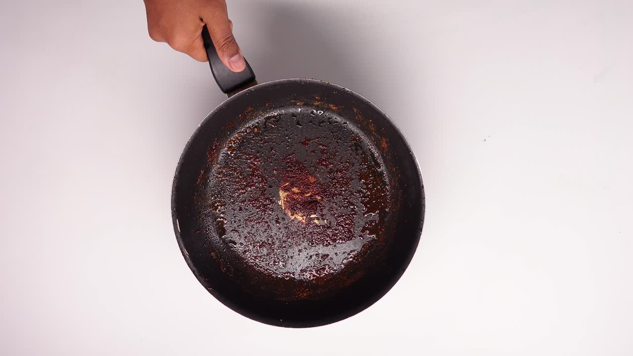 Hand Holding Dirty Frying Pan with Burnt Food Residue