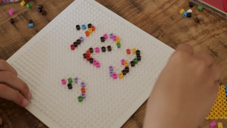 primer plano de las manos de una niña jugando con cuentas de colores y escribiendo números 1 2 3