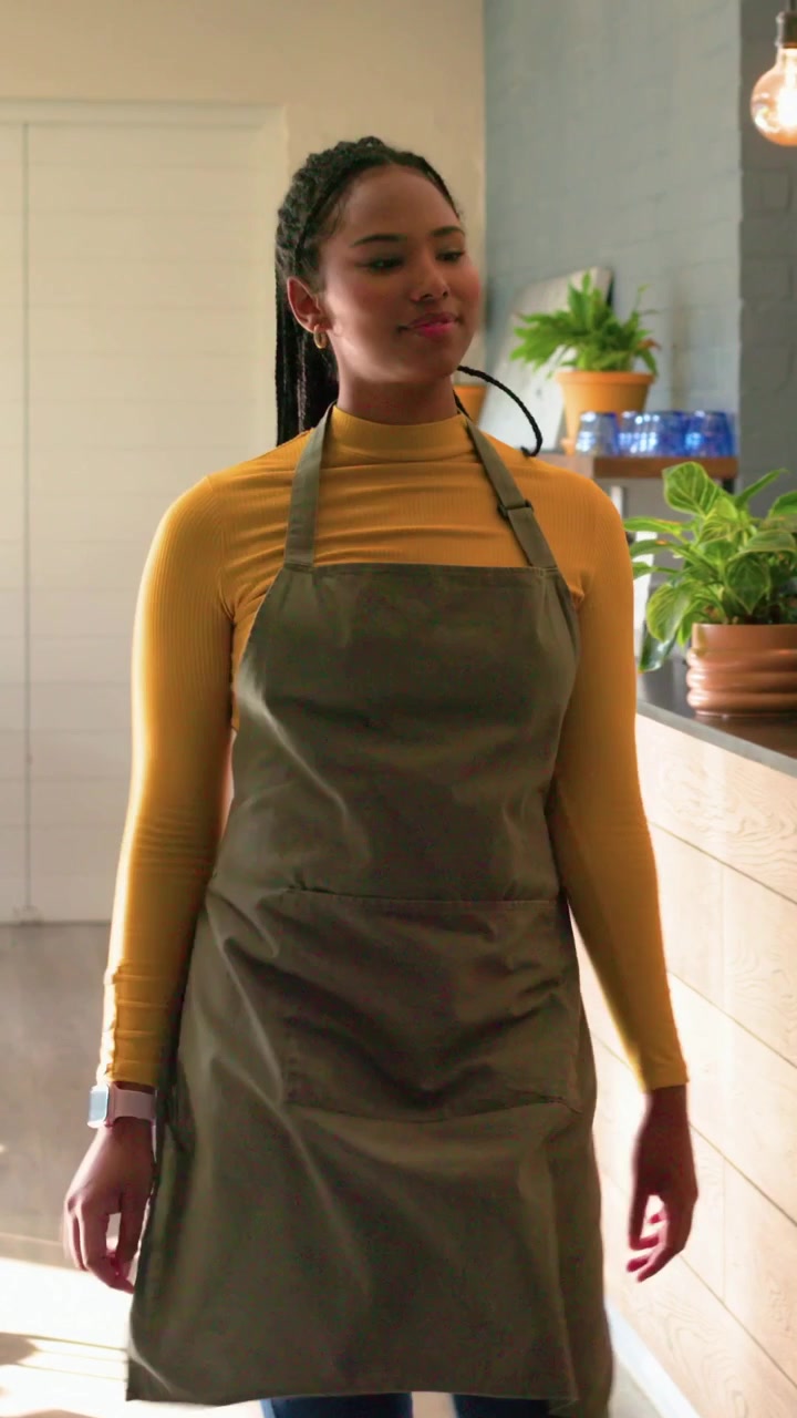 Vertical video: Handing cup, barista in olive-green apron, yellow top in cafe, walking to counter