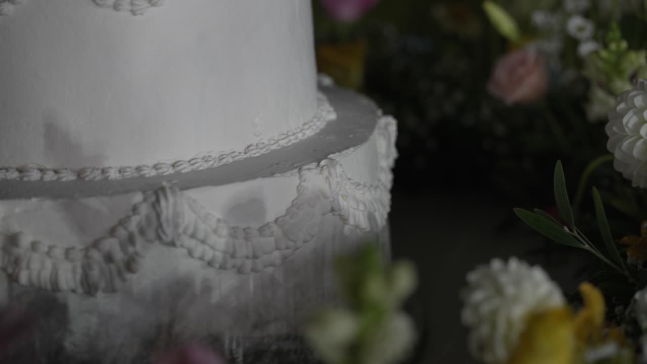 Nærbillede af hvid bryllupskage med pynt omgivet af fine blomster