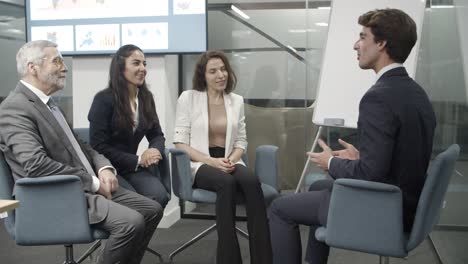 group of smiling employees sitting on chairs and talking