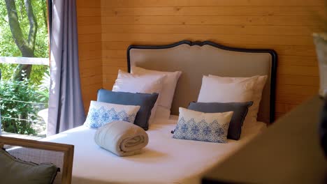 cozy cabin bedroom with white linens, blue pillows, wooden walls, and serene views