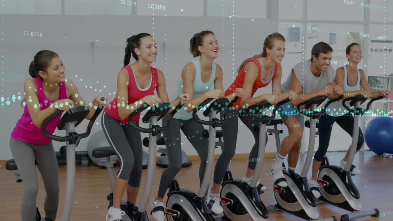 Group cycling on stationary bikes in fitness studio, displaying animated data points and overlays