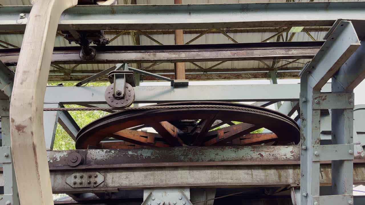 Static shot of a large pulley wheel rotating with steel cable inside a cable car system