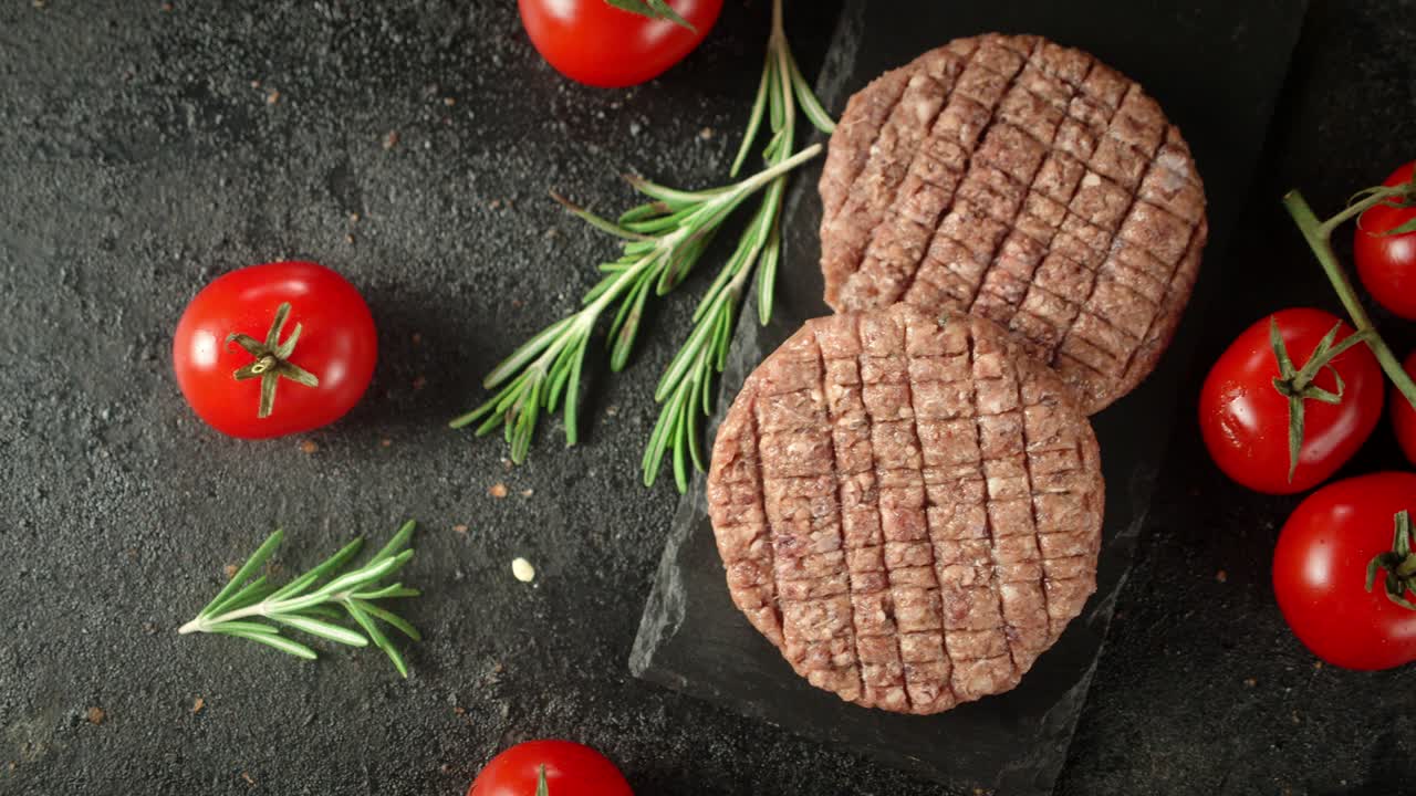 Raw burger meat on stone board with tomatoes and rosemary.