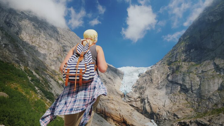 Eine aktive, erfolgreiche Frau steht auf einem Felsen und blickt auf die Berge und den darüber liegenden Gletscher