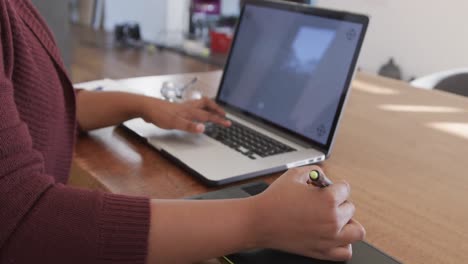 Midsection-of-african-american-plus-size-woman-using-laptop-and-graphic-tablet,-slow-motion