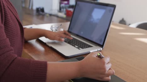 midsection of african american plus size woman using laptop and graphic tablet, slow motion