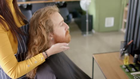 Caucasian-female-hairdresser-touching-beard-of-male-client-and-advising-at-salon,-in-slow-motion
