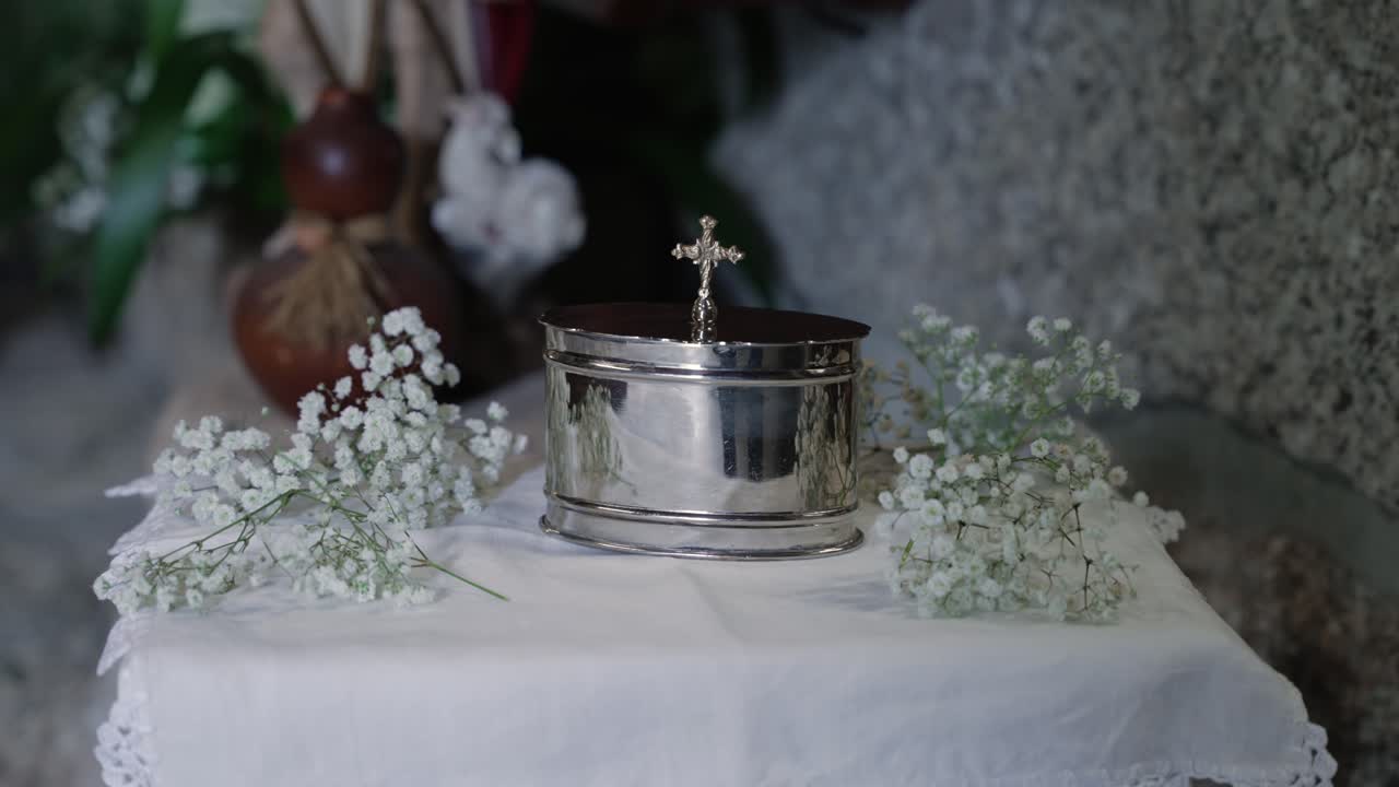 silver font with cross on white altar cloth surrounded by gypsophila flowers in church