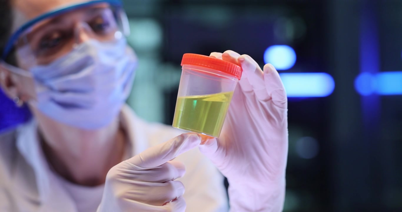 Woman scientist checks yellow liquid inside sample cup in lab