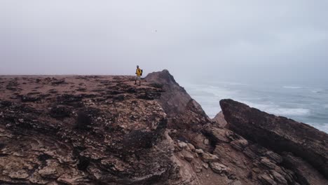 Man-standing-on-a-cliff-in-the-sea-in-a-foggy-weather-drone-clip