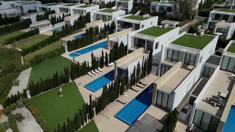 a descending drone shot reveals stunning villas and terraced houses, each with a private pool, elegantly aligned side by side in a luxurious setting.