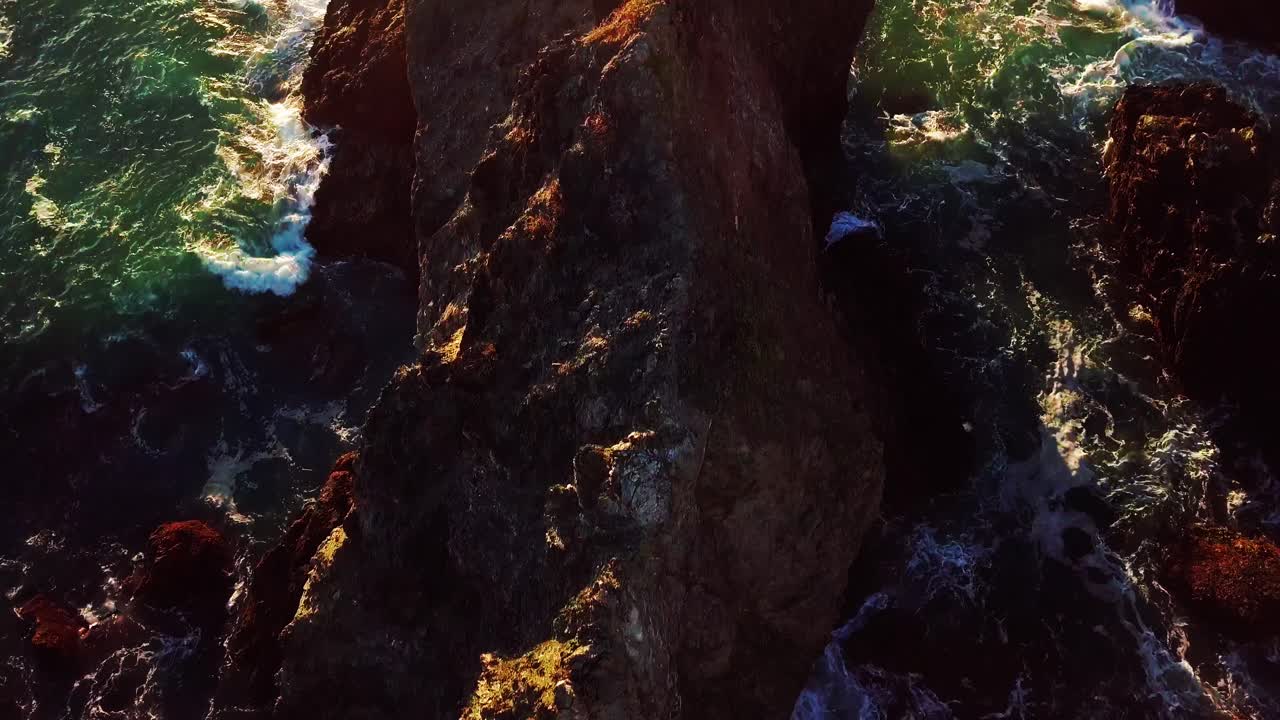 último sol do dia ilumina ondas verdes do oceano batendo em penhascos rochosos em big sur california
