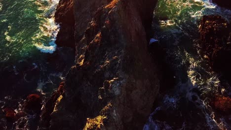 el último sol del día ilumina las olas verdes del océano chocando contra los acantilados rocosos en big sur california