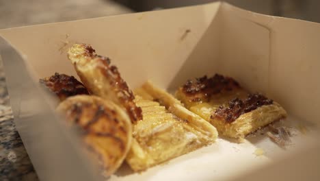 box of puff pastries with crispy edges, partially eaten, sitting on a countertop