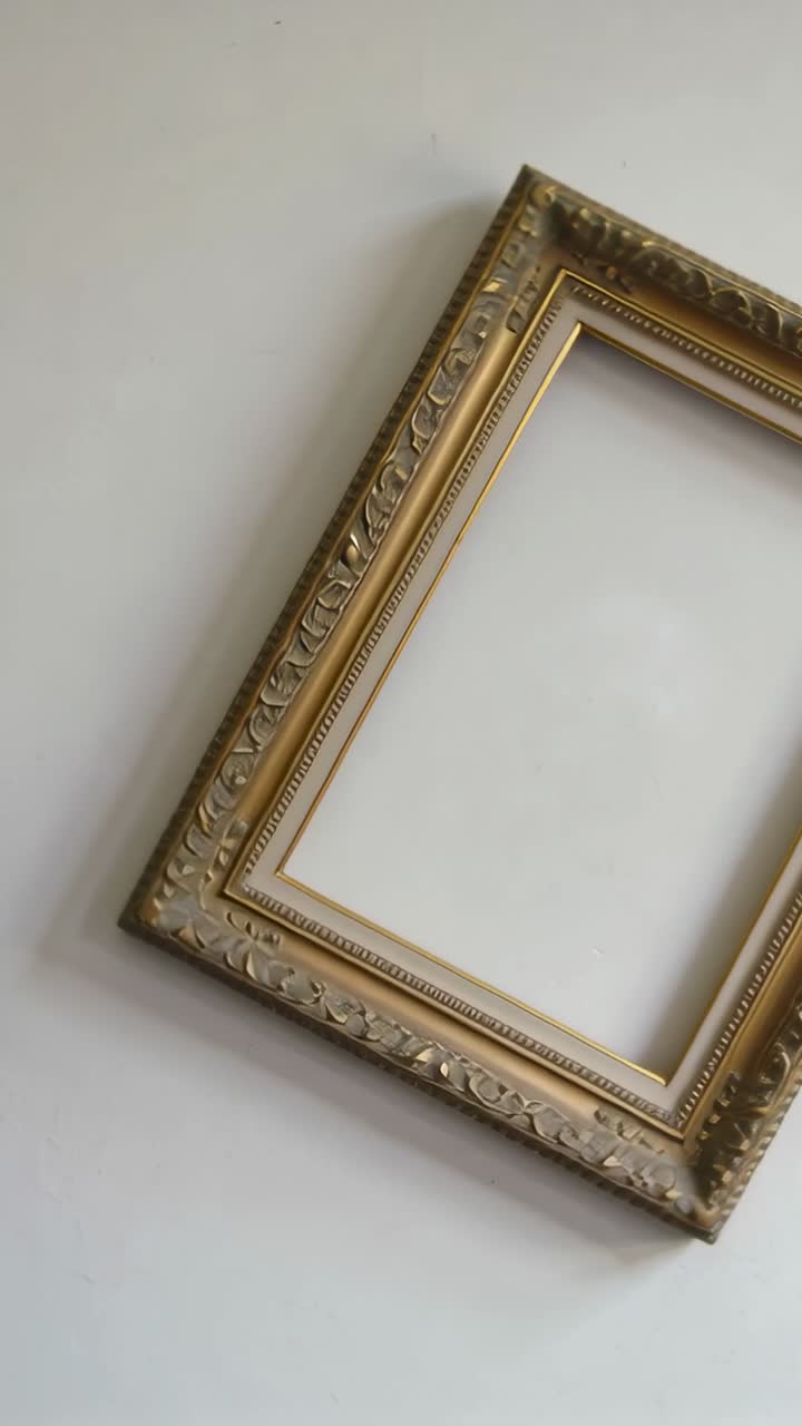 Vertical video: Camera rotating to reveal gilded frame on pale wall with empty backing, copy space