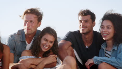 Grupo-De-Amigos-Sentados-En-La-Playa-Y-Hablando-Durante-Las-Vacaciones-De-Verano