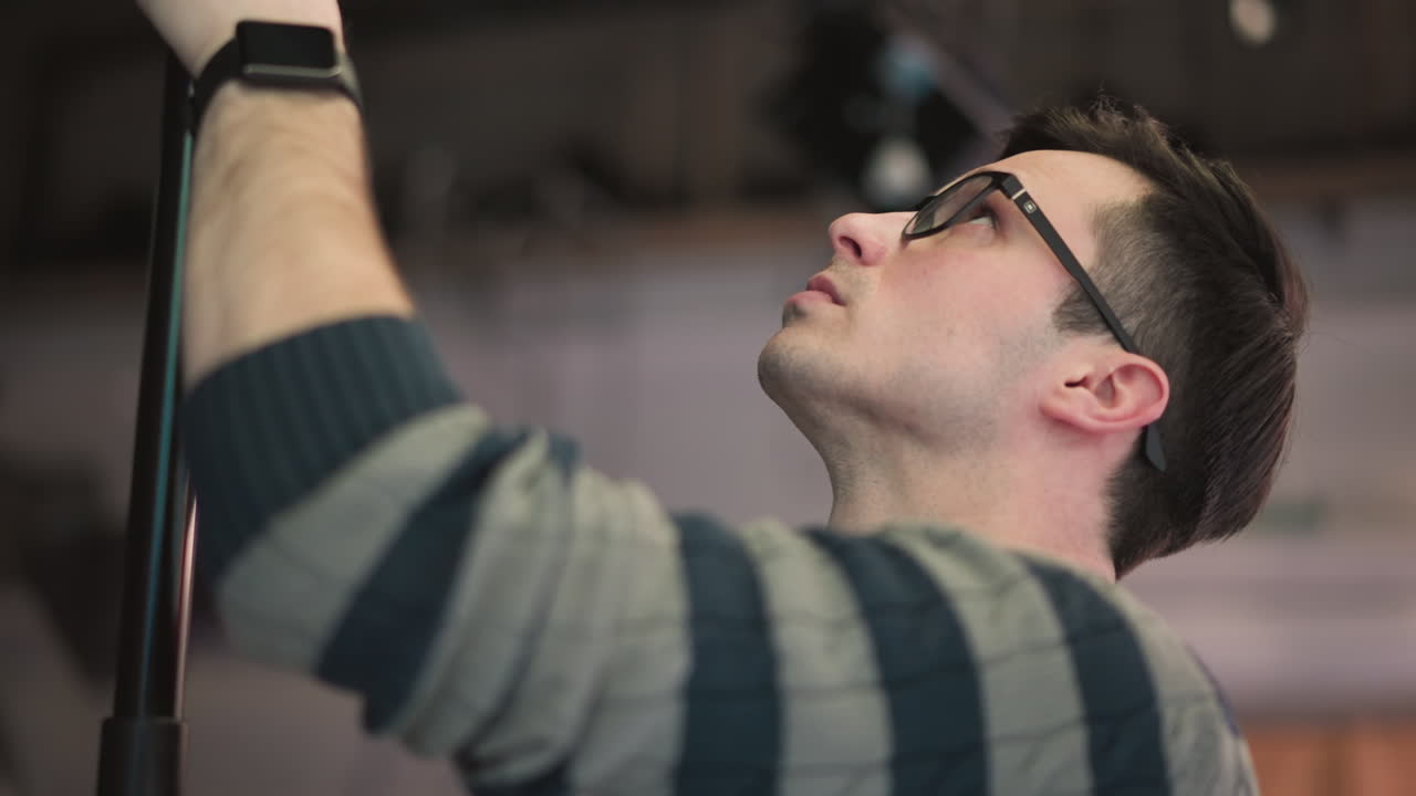 Close-up of man holding boom microphone, adjusting position during sound recording process in studio, focusing on equipment, preparing for video production with professional setup and crew