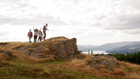 Un-Grupo-De-Cinco-Amigos-Adultos-Jóvenes-Felices-Llegan-A-La-Cumbre-Animando-Con-Los-Brazos-En-El-Aire-Y-Abrazándose-Durante-Una-Caminata-Por-La-Montaña