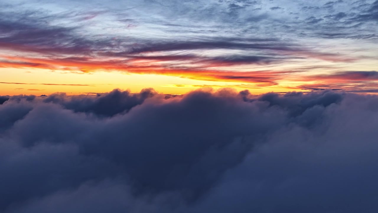 Colorful sunrise paints the sky in vibrant hues above a sea of rolling clouds. Ideal for atmospheric scenes or nature documentaries.