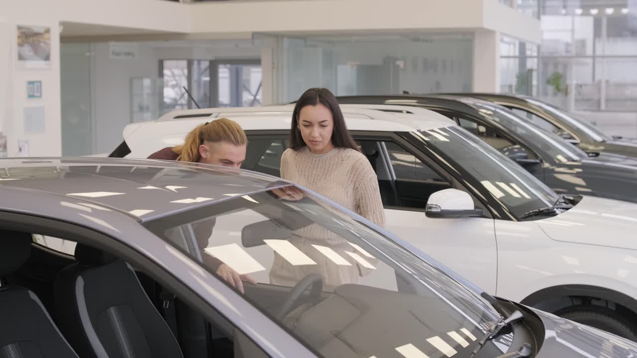 una hermosa pareja de jóvenes en la sala de exposición de automóviles eligiendo un coche nuevo para comprar.