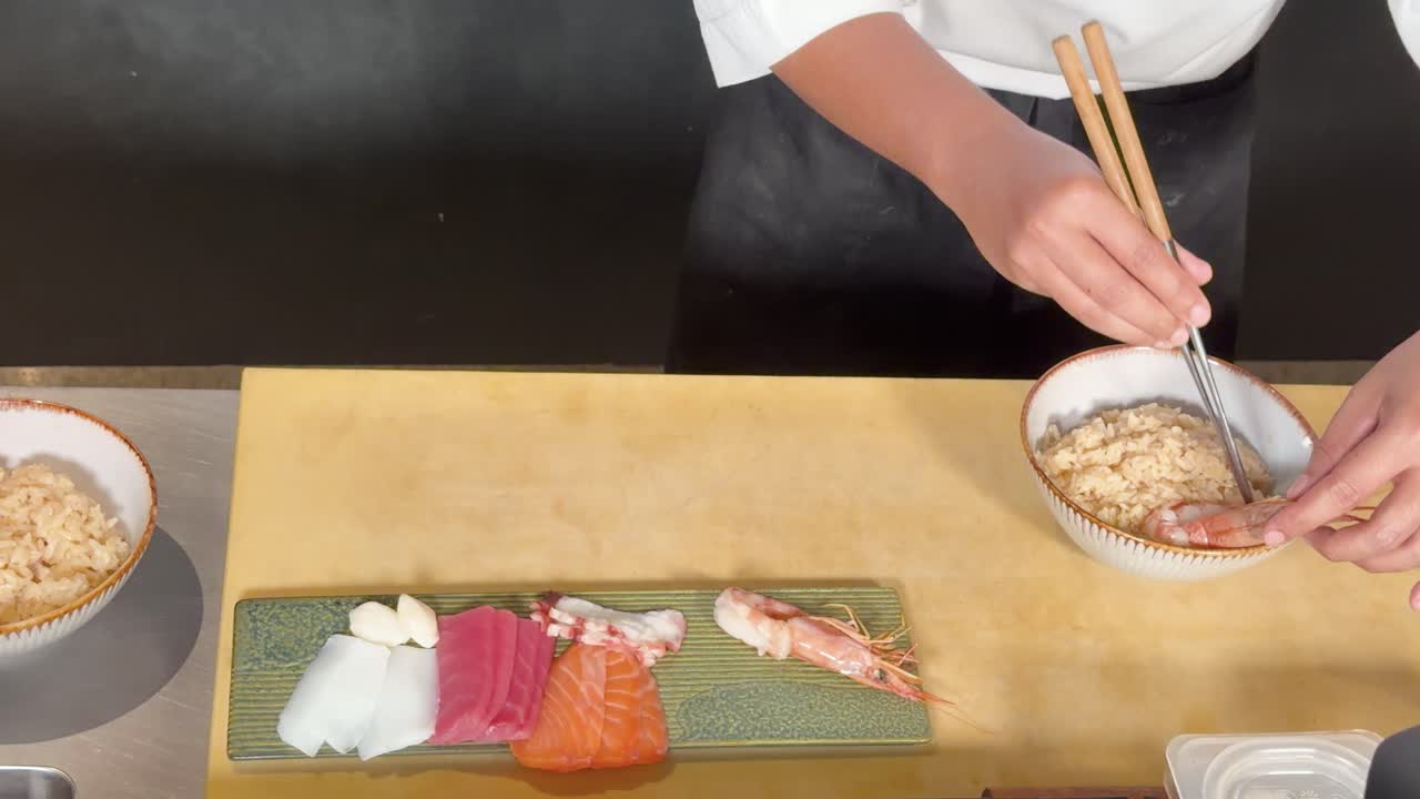 Pohled shora na sushi šéfkuchaře míchajícího rýži ochucenou vedle barevného talíře sashimi omakase