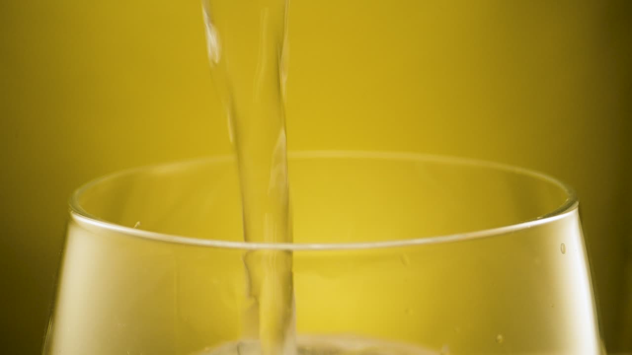 Primo piano estremo che riempie un bicchiere con acqua di rubinetto cristallina, sfondo giallo