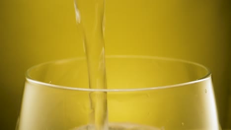 Extreme-close-up-filling-a-glass-with-crystal-clear-tap-water,-yellow-background